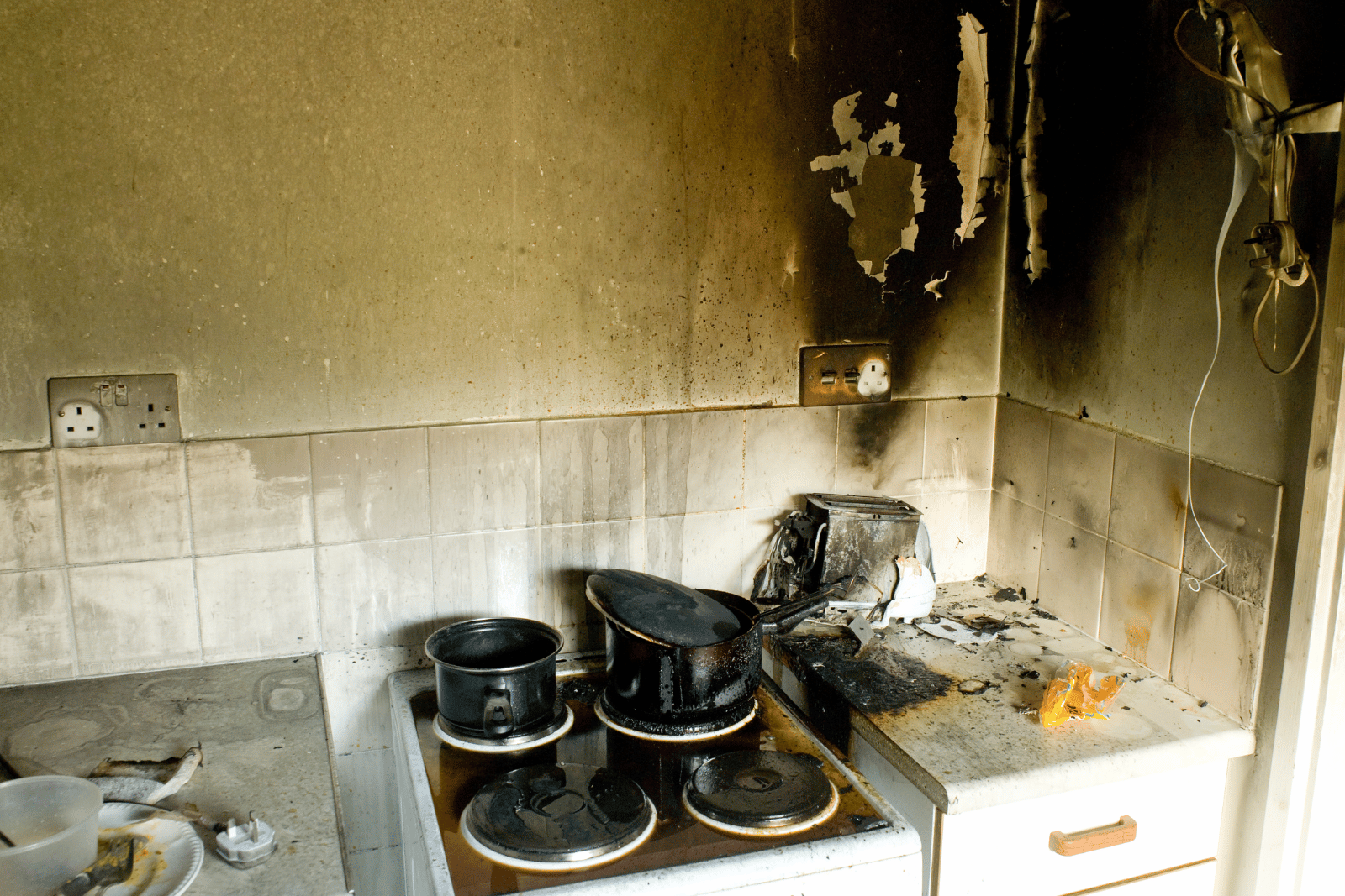 Kitchen with blackened walls, damaged appliances, and soot-covered surfaces.