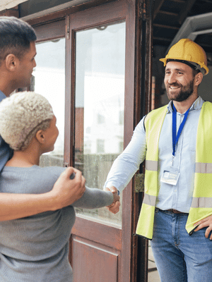 Three people shaking hands at a doorway; one wears a yellow hard hat and reflective vest.