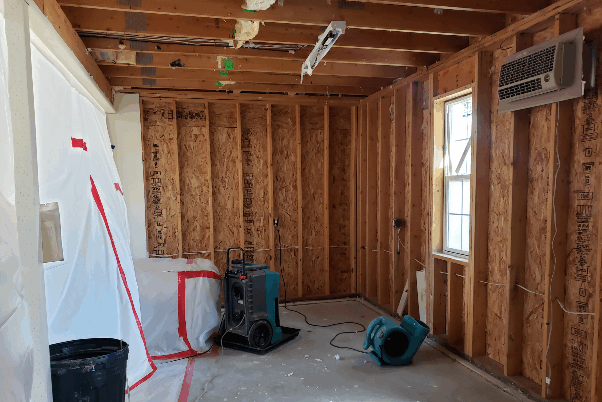 Room with exposed wooden walls, a blue air mover, and drying equipment.