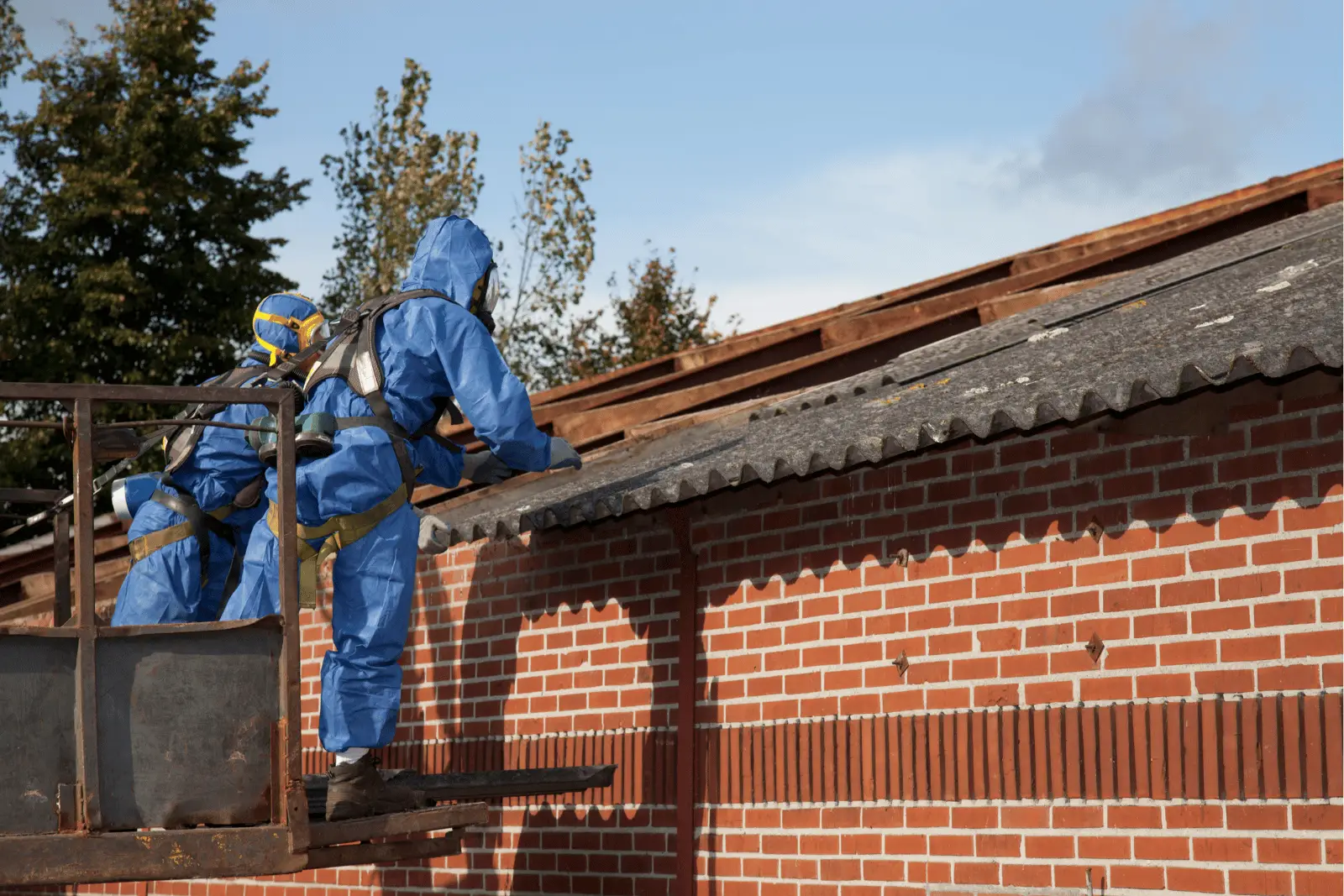 Two workers in blue protective gear inspecting a roof from a platform.