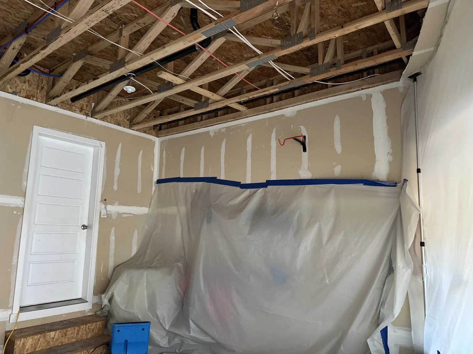 Opened ceiling framing above a plastic containment barrier and drying equipment