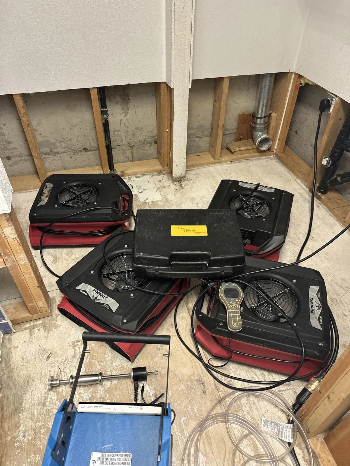 Several air movers and restoration tools beside an opened interior wall