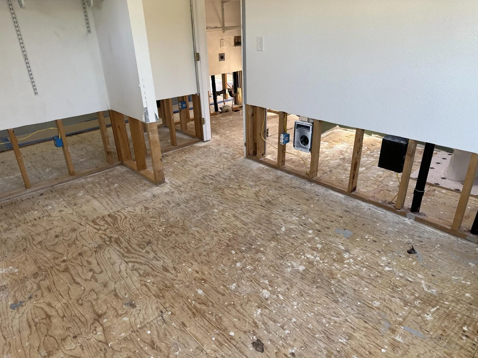 Selective drywall removal exposes wall framing above an uncovered wood subfloor